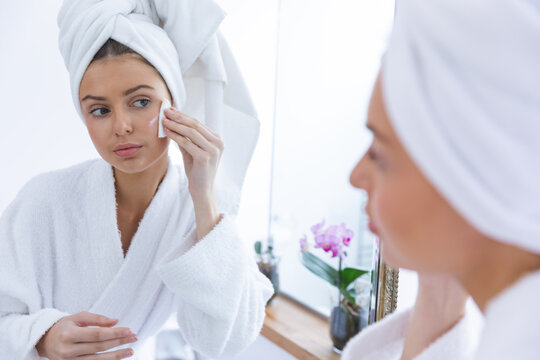 Woman in bathrobe removing make up with cotton pad while looking in the mirror