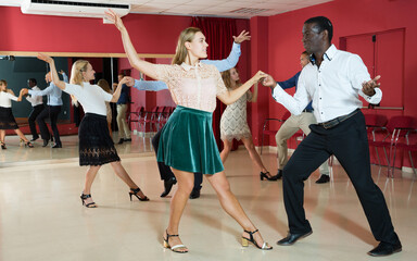 Adult dancing couples enjoying active boogie-woogie in modern studio..