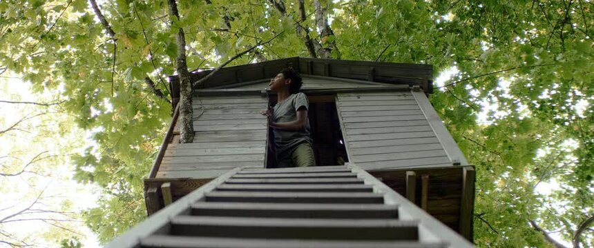 African-American kid boy talking to someone while playing in a tree house. Shot on RED Dragon with 2x Anamorphic lens