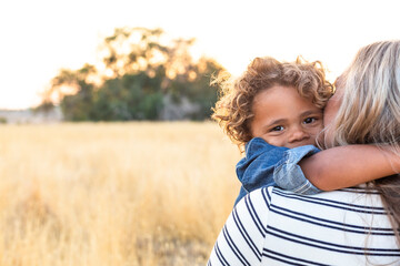 The face of an adorable curly haired African American boy in the arms of his mother in the outdoor...