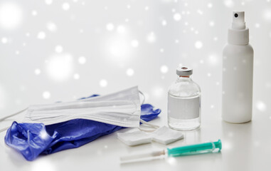 medicine and healthcare concept - close up of syringe, drug, wound wipes, hand sanitizer with gloves and mask on table in winter over snow