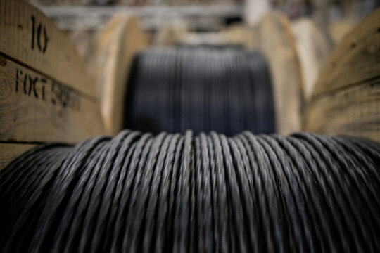 Vertical coils ndustrial wires. Many turns of main electrical cable is closeup. Roll of outdoor fiber optic signal shielded cables. Wooden Coils of powerful black telecommunications wire