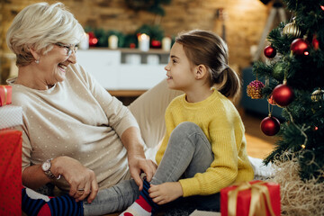 Happy senior woman and her granddaughter talking while relaxing at home on Christmas.