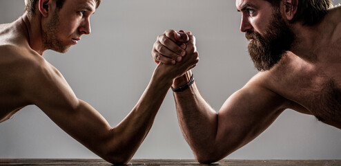 Two man's hands clasped arm wrestling, strong and weak, unequal match. Heavily muscled bearded man...