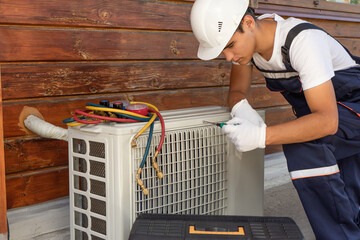 A young master in a white construction helmet repairs air conditioning, installation of split...