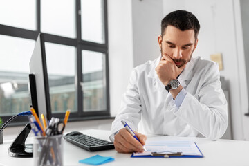 healthcare, medicine and people concept - stressed male doctor with clipboard at hospital