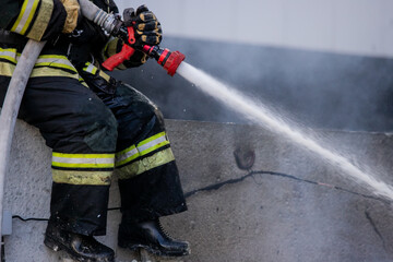 Firemen using extinguisher and water from hose for fire fighting in firefight training. Firefighter wearing fire suit for protect and safety under danger case.This team is under civil service system.