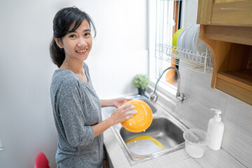 Beautiful smiling young woman washing the dishes in kitchen