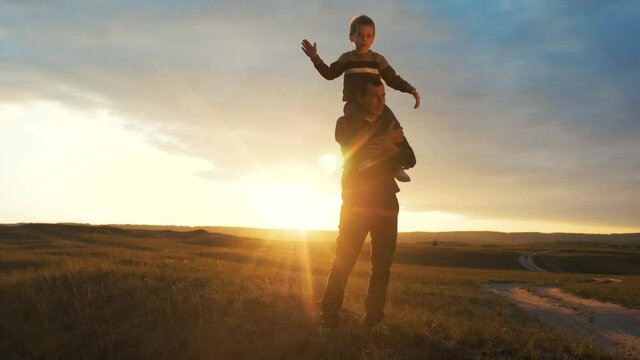 happy family. son sits on his neck teamwork at father shows hands to the side plays at the pilot depicts an airplane silhouette at sunset. happy family concept childhood lifestyle man dad with little