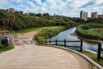 Cement Pathway Leading to Side of River with Builidngs in Background
