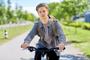 Obraz premium lifestyle, transport and people concept - young man or teenage boy with backpack riding bicycle on city street