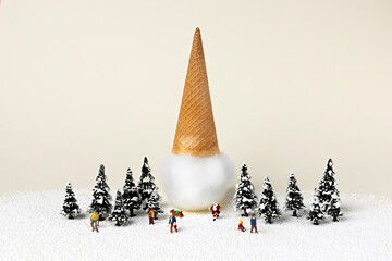 Christmas creative layout made with tiny trees, miniature people and ice cream cone on vanilla snow...