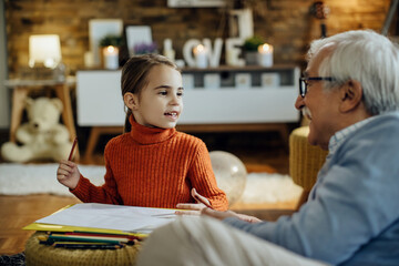 Happy little girl talking to her grandfather while coloring at home.