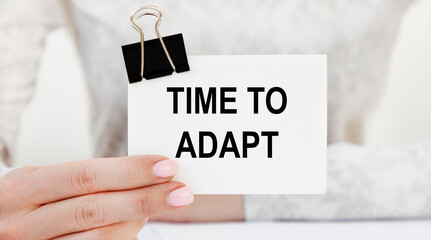 The girl holds a card with the text TIME TO ADAPT.
