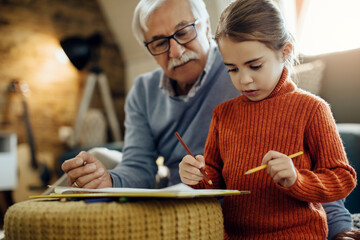 Little girl drawing while spending time with grandfather at home.