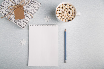 A clean notebook lies on a light background, next to a pencil, a mug with coffee and a gift. For recording ideas, planning, summing up the results of the year. Horizontal photo.