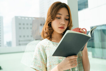 Beautiful young asian woman read a book and drink a cup of coffee.