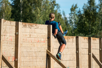 Obraz na płótnie Canvas Woman climbing over a wooden wall at an obstacle course race
