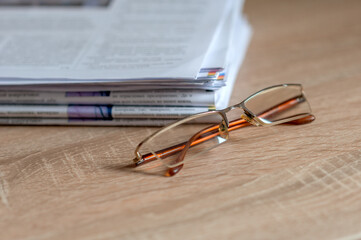 stack of newspapers and reading glasses on the table neutral background