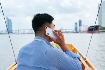 Fototapeta na wymiar Back view - Asian business man talking on the phone travel by a boat in Bangkok.