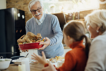 Happy senior man bringing Thanksgiving turkey to dining table.