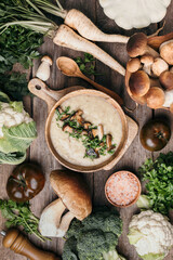 Homemade vegetarian mushroom soup with fried mushrooms, vegetables, spices, raw boletus edulis mushroom on wooden background. Top view. Copy space. Autumn harvest concept