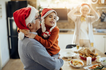 Happy little girl ad her grandfather embracing while spending Christmas day together at home.