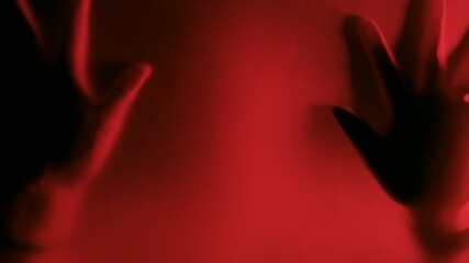 Defocused Possessed people scratching glass with hands with red light background, creepy silhouette, horror. Scary ghostly creature behind the glass, Hand hits the matte glass surface
