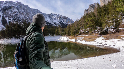 Fototapeta na wymiar Man walking around the shore of Green Lake, Austria and taking a selfie. Powder snow covering the mountains and ground. Soft reflections of Alps in calm lake's water. Winter landscape of Austrian Alps