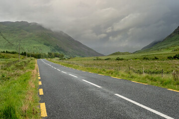 Narrow empty asphalt road into mountains, Low cloudy sky over peaks. Nobody, Connemara, Ireland. Concept travel, road trip
