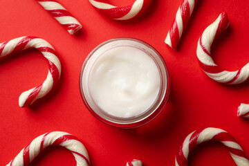 Jar of cosmetic cream and candy canes on red background