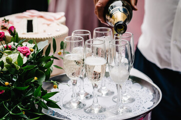 Waiter pouring Champagne in glasses on the tray. Party and holiday celebration concept.
