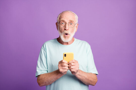 Photo Portrait Of Shocked Old Man Holding Phone In Two Hands Isolated On Vivid Violet Colored Background