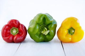 Red, green and yellow peppers on a white wooden table