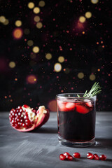 Pomegranate Christmas cocktail with champagne, club soda and rosemary on black table. Xmas drink