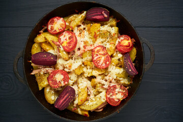 Cooked potato, baked with tomatoes, bacon and cheese in a pan.