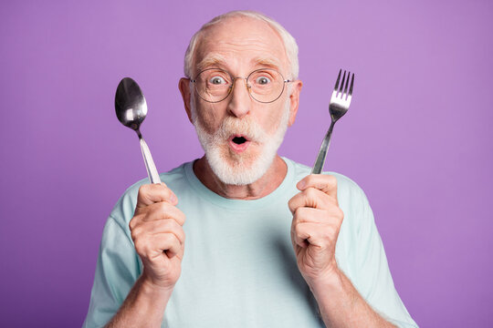 Photo of surprised old man hold fork spoon open mouth wear blue t-shirt isolated over violet color background