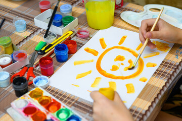 Obraz na płótnie Canvas a girl drawing watercolor a big smiling sun on a blank white paper, artistic creation at home, makes creative artwork