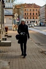 Woman traveler in a coat is walking with a camera along a city street.