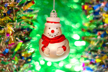 Vintage glass Soviet New Year's toy (snowman) against the background of a Christmas tree and colorful bright tinsel.
