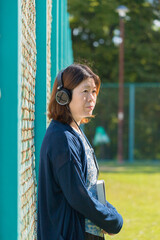 Fototapeta premium 朝の公園のグランドで本を持ってヘッドホンで音楽を聴いている女性の姿