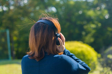 秋の公園でヘッドホンで音楽を聴いている中年女性