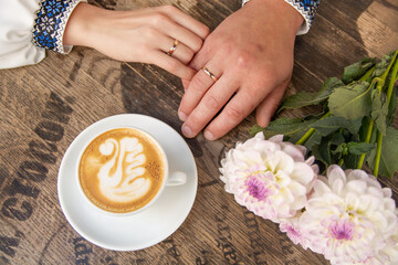 Wedding rings on the hands of brides. Fragrant, hot cappuccino on the table.