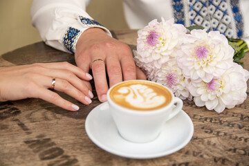 Wedding rings on the hands of brides. Fragrant, hot cappuccino on the table.
