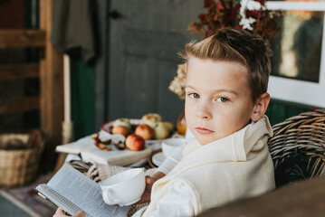 a boy in armchair reading book on the porch on the backyard with autumn decorations