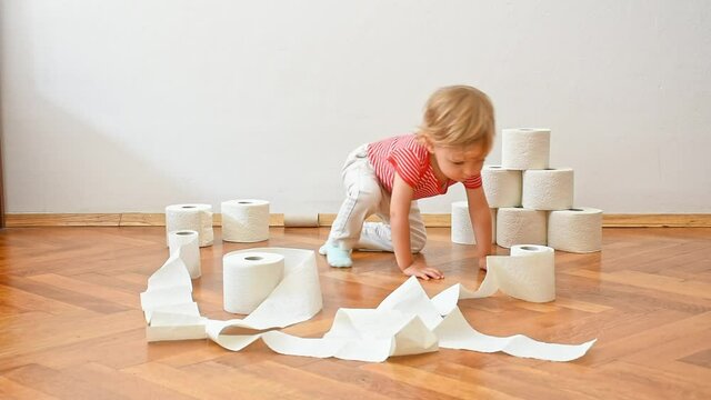 Cute little child sitting on the floor and having fun playing with toilet paper