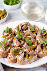 Anchovies toasts and two glasses of white wine on worn wooden table top, vertical image