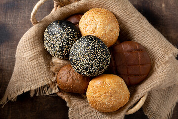 Sesame buns for burgers. Wheat and rye rolls in a basket on a brown wooden background. Homemade buns with sesame seeds. The view from the top. Copyspace