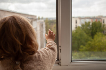 The child climbs to the window, the girl on the window sill rests on the net, the danger of falling. The child is alone at home, can fall out of the window.
