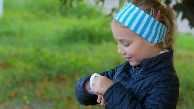 Child using smartwatch outdoor in autumn park. Kid talking on vdeo call on the smartphone. Schoolgirl using touchscreen display on watches browsing internet. Smart kids wristwatch with GPS tracker.